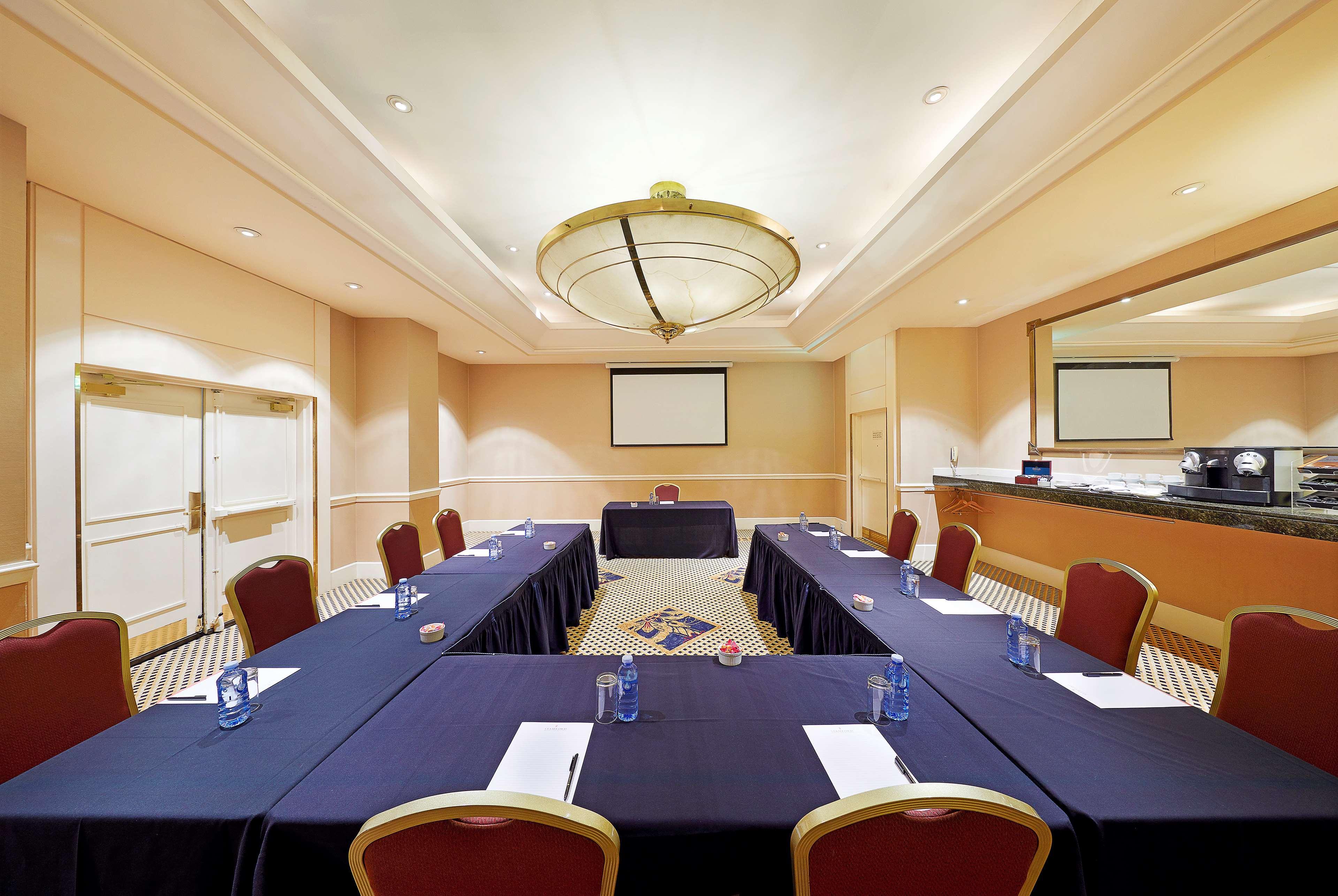 Stamford Plaza Sydney Airport Hotel & Conference Centre Exterior photo The photo shows a conference room set up for a meeting. The room features rectangular tables arranged in a U-shape, covered with dark blue tablecloths. Each table has a notepad and a pen placed on it, along with a glass of water. There's a prominent 