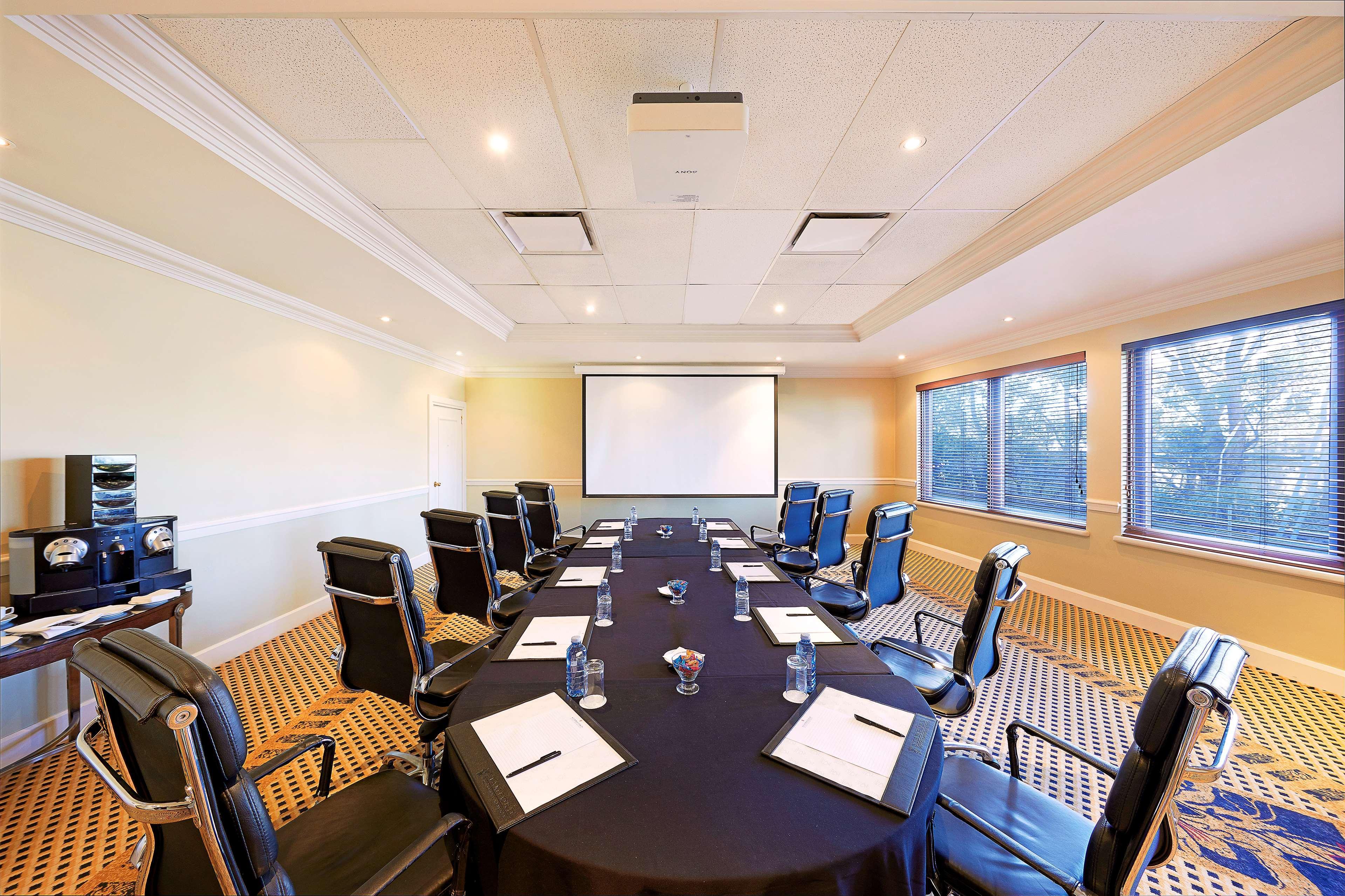 Stamford Plaza Sydney Airport Hotel & Conference Centre Exterior photo The photo shows a conference room set up for a meeting. There is a large, oval table covered with a black tablecloth, with several empty notebooks and glass water bottles placed in front of each chair. Around the table, there are multiple black leath