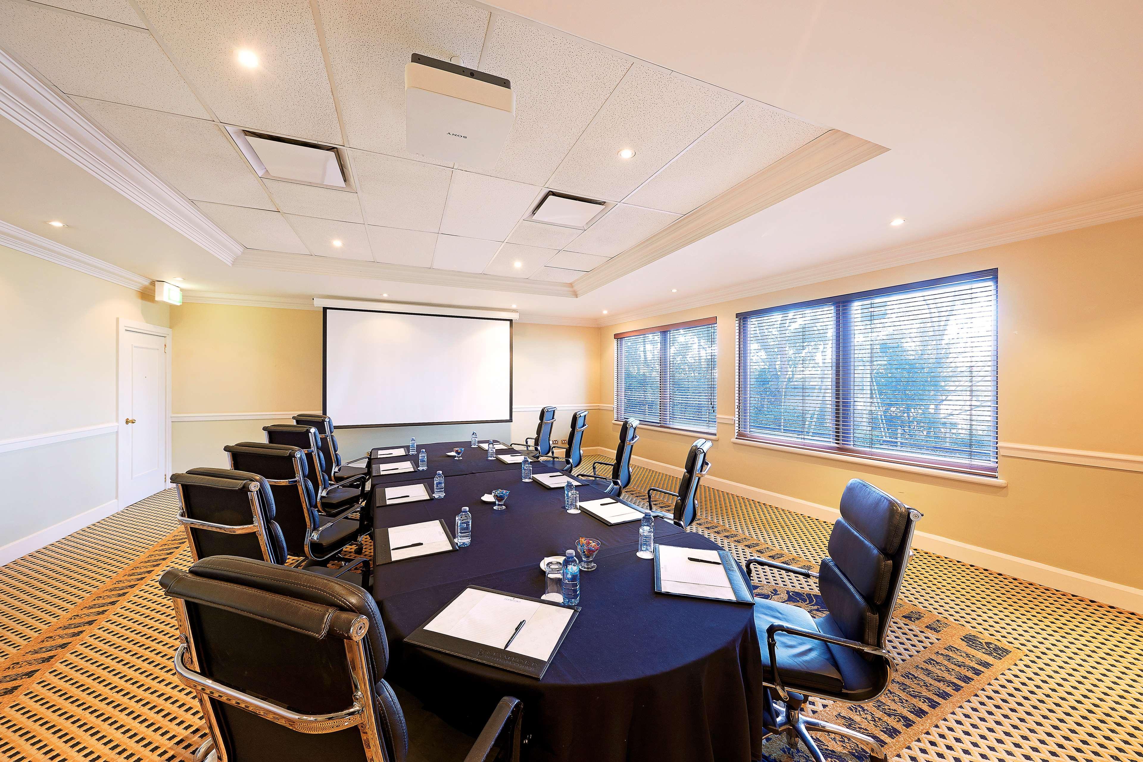 Stamford Plaza Sydney Airport Hotel & Conference Centre Exterior photo The photo shows a meeting room with a large round table covered in a black tablecloth. Around the table, there are several black leather chairs. On the table, there are sheets of paper, presumably for notes, and glasses of water. A projector screen i