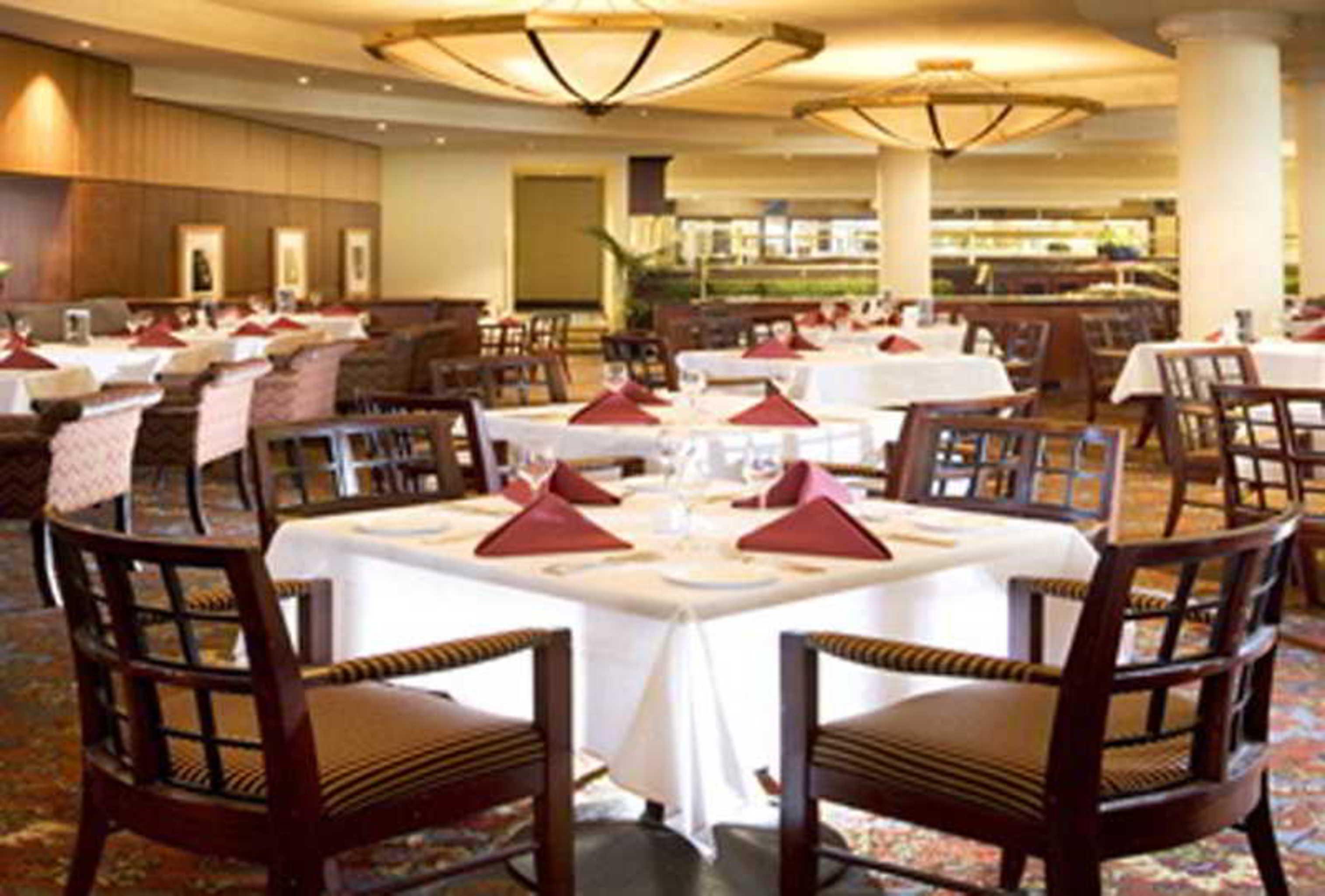 Stamford Plaza Sydney Airport Hotel & Conference Centre Restaurant photo The photo shows an elegantly designed restaurant interior. It features several tables with white tablecloths, set for dining with neatly folded red napkins. The chairs are made of dark wood and have a classic style. The lighting is warm, coming from 