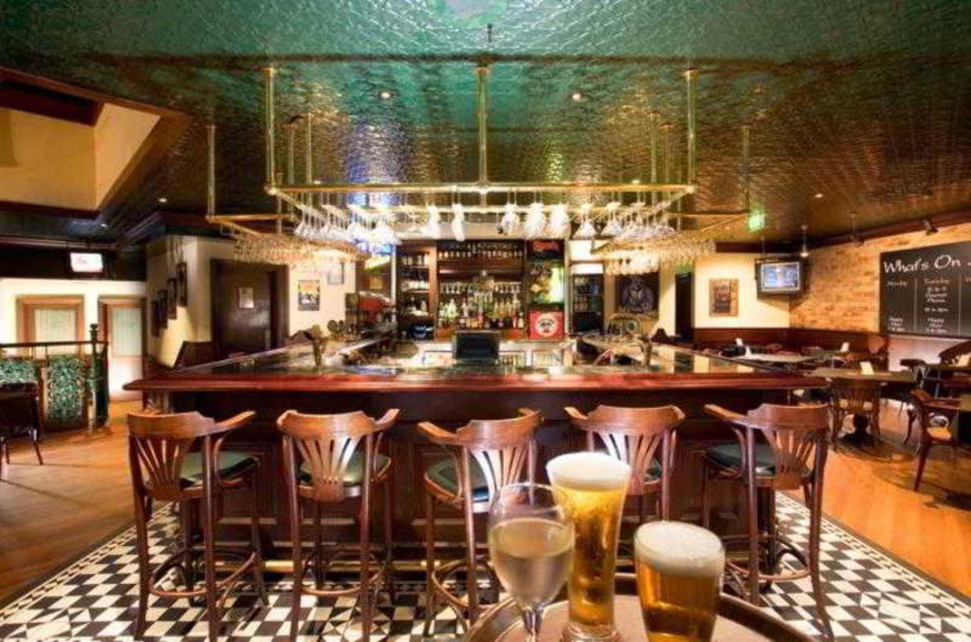 Stamford Plaza Sydney Airport Hotel & Conference Centre Restaurant photo The photo depicts a pub or bar interior. It features a wooden bar with several high-backed stools arranged around it. Behind the bar, there are shelves stocked with various bottles, suggesting a wide selection of drinks available. The ceiling is an a