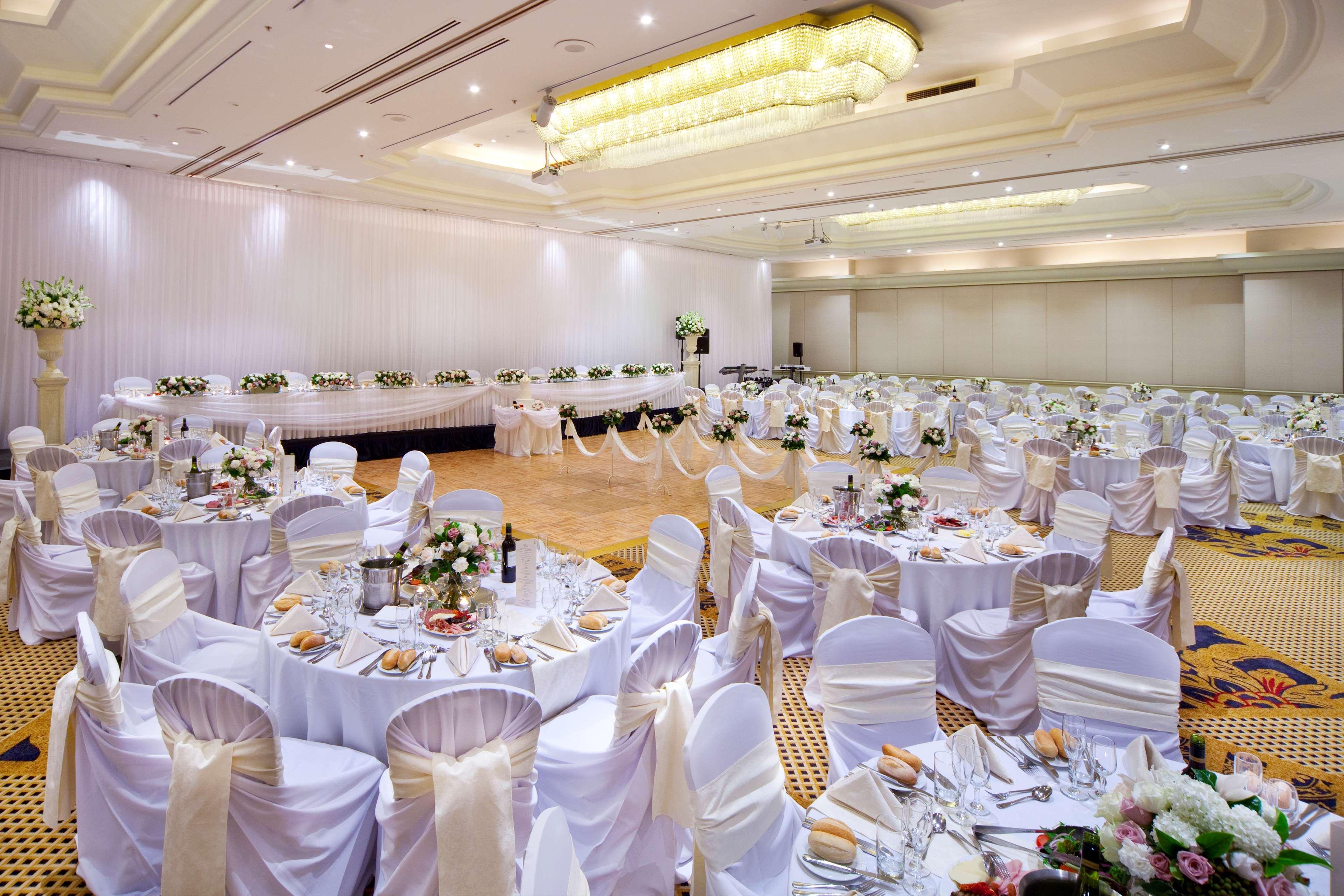 Stamford Plaza Sydney Airport Hotel & Conference Centre Exterior photo The photo shows a beautifully arranged banquet hall designed for a formal event, such as a wedding or a reception. The room features numerous round tables, each covered with white tablecloths and elegantly draped chairs, accented with light-colored s