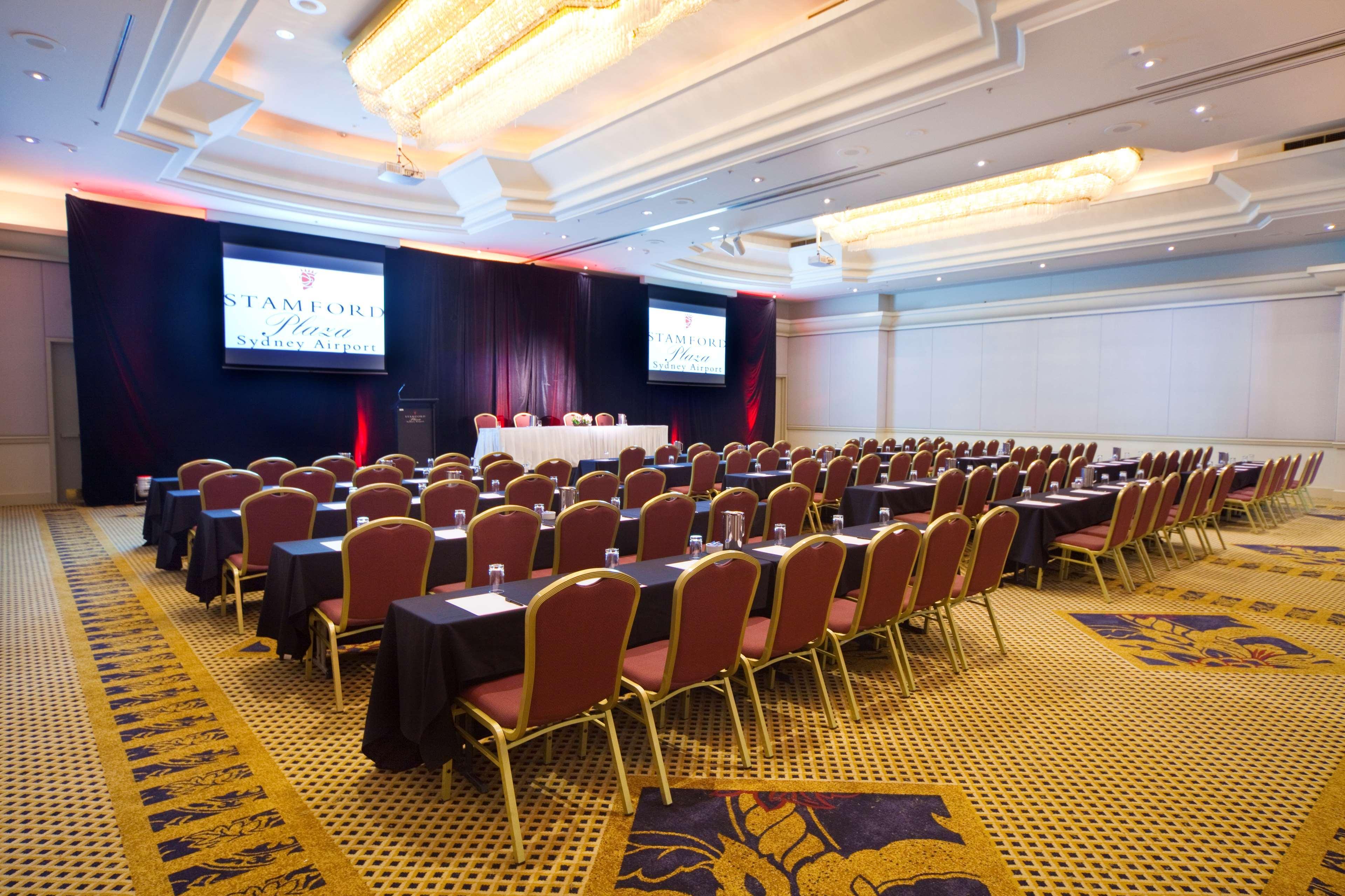 Stamford Plaza Sydney Airport Hotel & Conference Centre Exterior photo The photo shows a conference or meeting room set up for an event. There are several rows of chairs arranged facing a stage or table at the front. The chairs are gold with red upholstery. A long table covered with a white cloth is positioned at the fr
